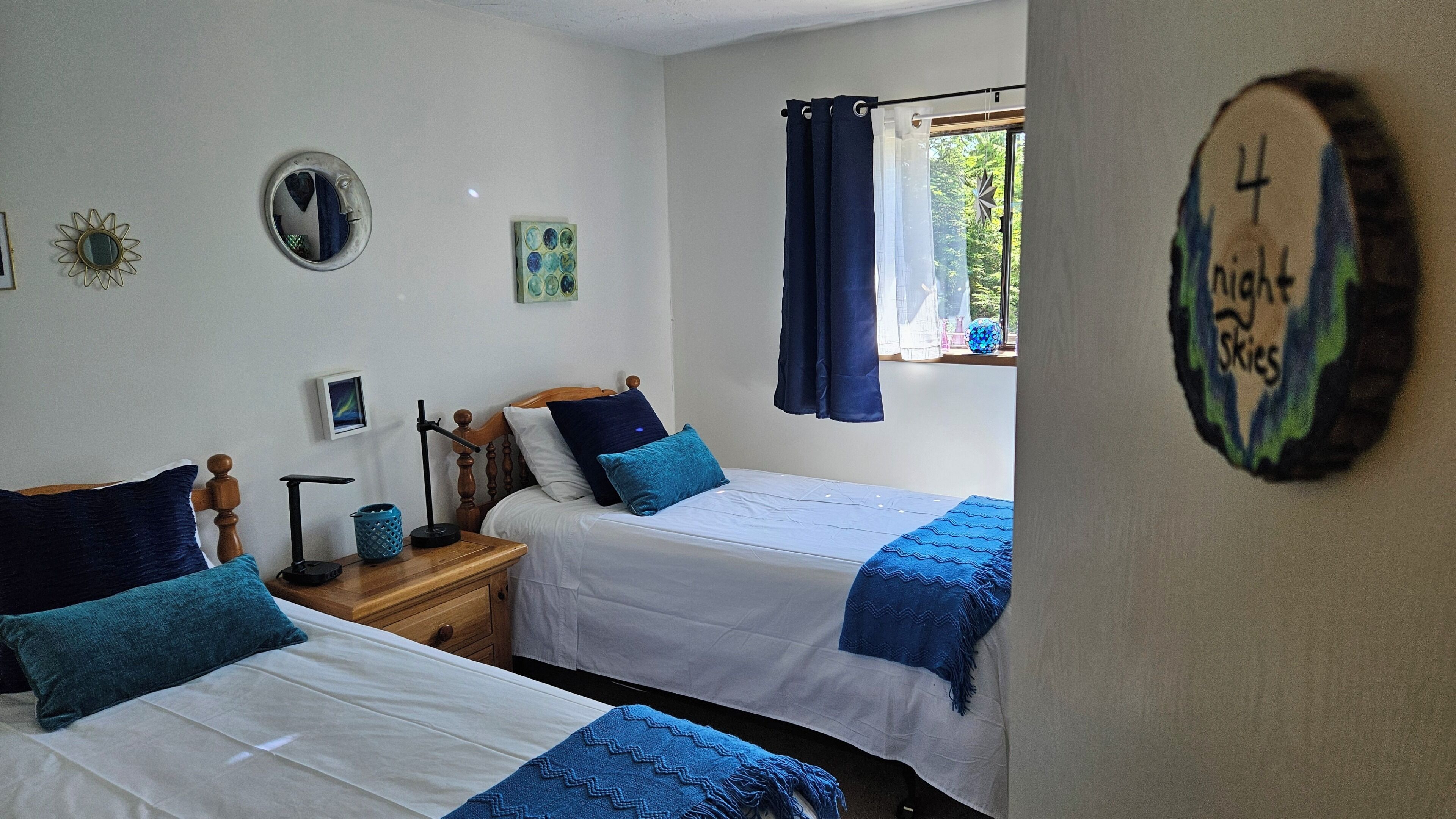 Une chambre avec deux lits, une table de chevet, un miroir et une fenêtre avec des rideaux.
