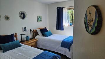 Une chambre avec deux lits, une table de chevet, un miroir et une fenêtre avec des rideaux.