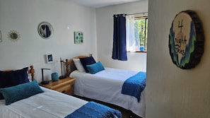 A bedroom with two beds, a nightstand, a mirror, and a window with curtains.