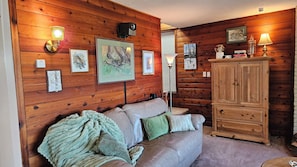 A cozy room with a wooden wall, a leather sofa, a cabinet, and framed artwork.