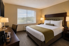 Una habitación de hotel con cama, escritorio, silla, televisor y ventana con persianas.