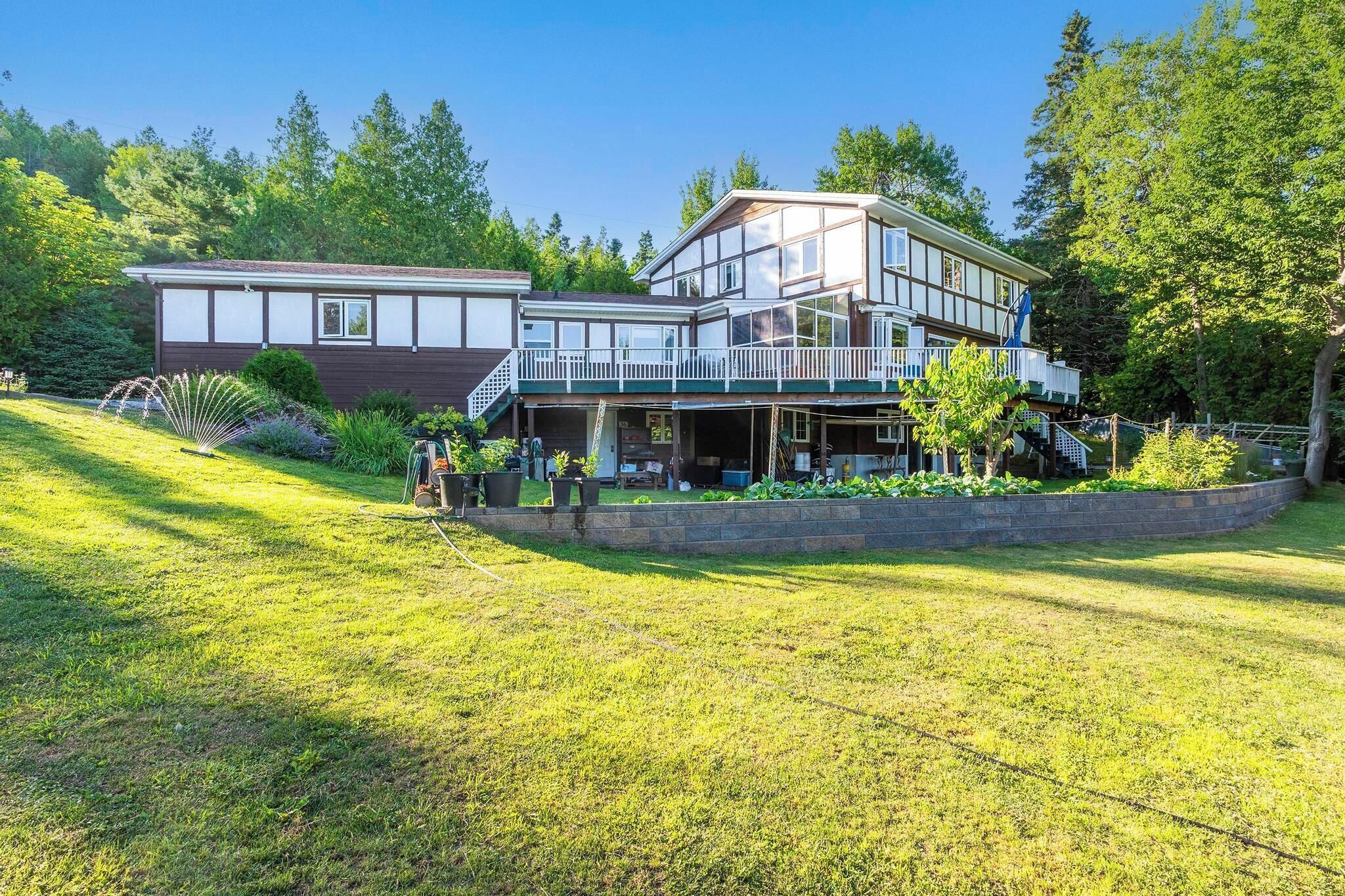 Ein zweistöckiges Haus mit Balkon, umgeben von einem gepflegten Rasen und Bäumen.
