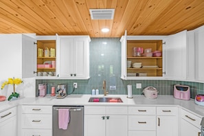 A modern kitchen with white cabinets, a stainless steel sink, and a wooden ceiling.