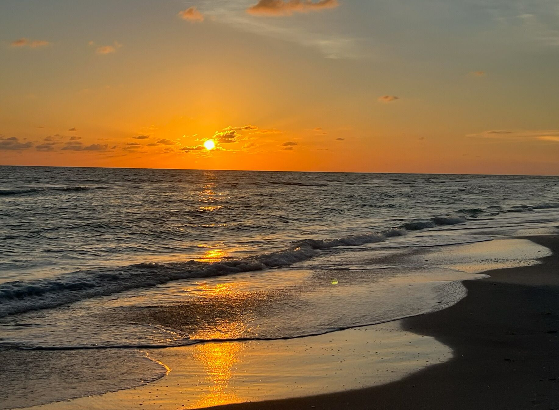 Une plage avec des vagues, un coucher de soleil et un ciel dégagé.