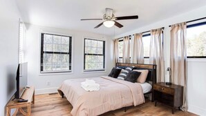 A bedroom with a bed, a ceiling fan, two windows with blinds, a bedside table, and a TV on a stand. - 2 Bedroom Modern Lake House Close to Midtown (College Park)