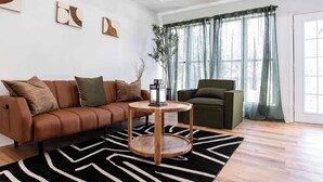 A modern living room with a brown leather sofa, a green armchair, a round wooden coffee table, and a black and white rug. - 2 Bedroom Modern Lake House Close to Midtown (College Park)