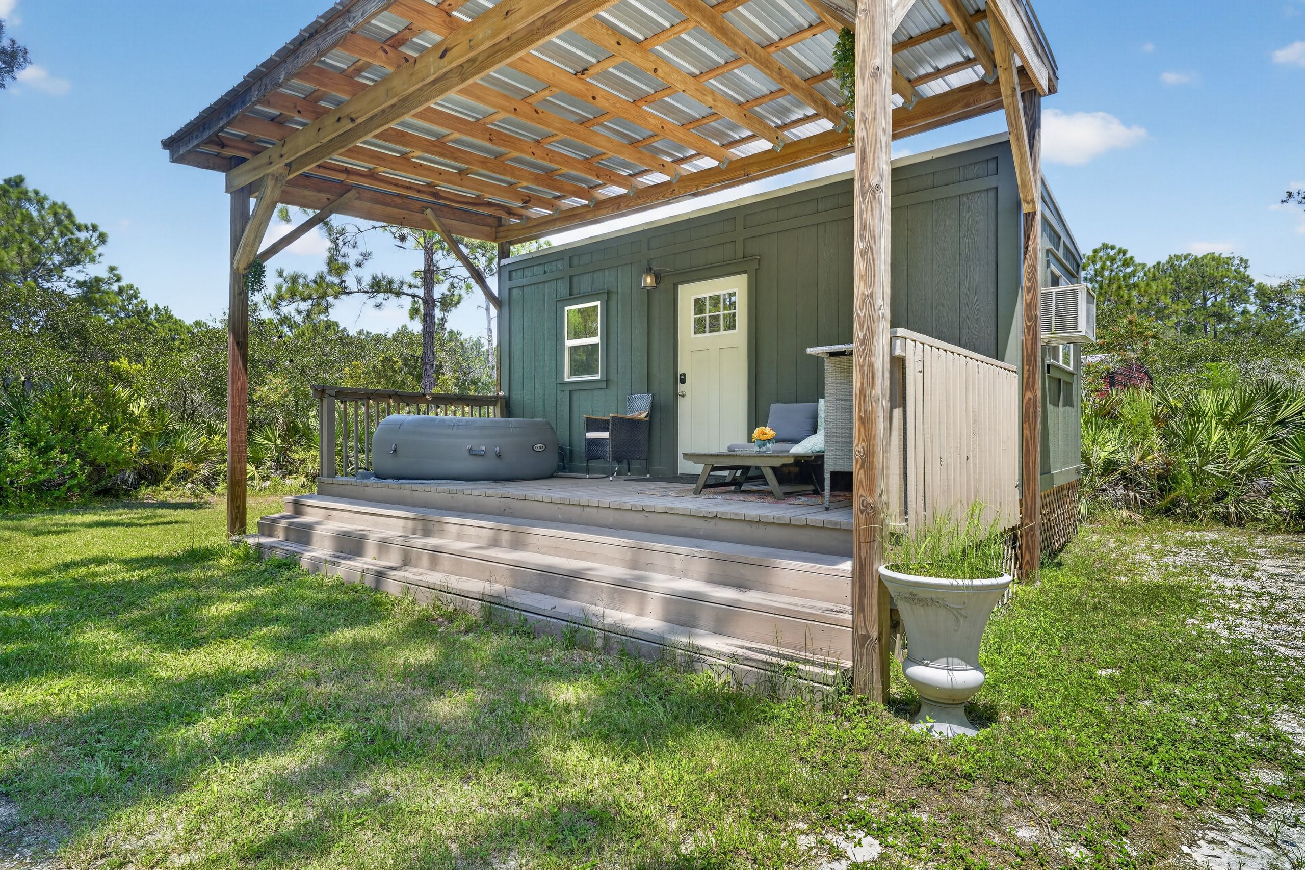 Un espacio al aire libre cubierto con una terraza de madera, una puerta y una pequeña zona de estar con mesa y sillas.