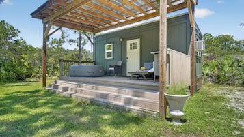 Un espacio al aire libre cubierto con una terraza de madera, una puerta y una pequeña zona de estar con mesa y sillas.