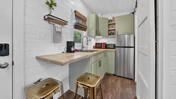 Una cocina compacta con encimera de madera, un refrigerador de acero inoxidable y un microondas rojo.