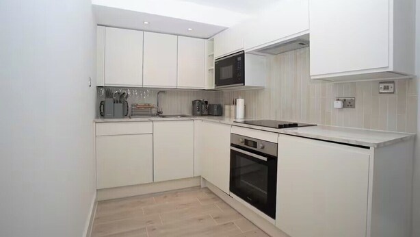 A compact kitchen with white cabinetry, a microwave, a stove, and a dishwasher. - Basement Flat Sleeps 3 with Patio (London)