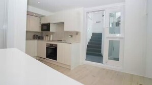 A compact kitchen with a microwave, oven, and cabinets. A staircase leads to an upper level. - Basement Flat Sleeps 3 with Patio (London)