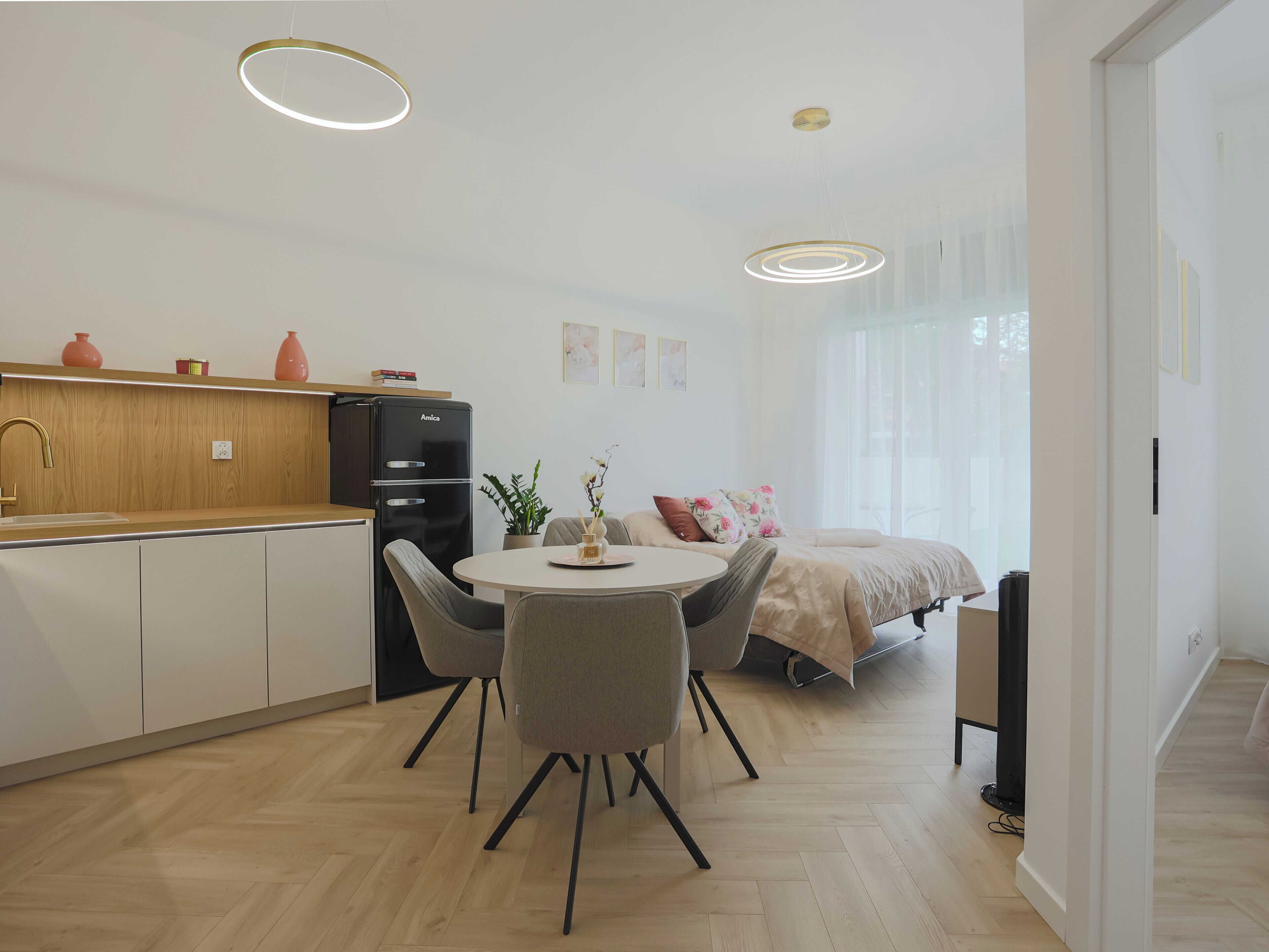 A modern kitchen with a refrigerator, sink, and wooden countertop. There is a dining area with a round table and chairs.