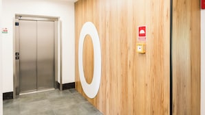 Un ascensor, una pared de madera con una letra 'O' blanca grande y un letrero de alarma de incendios.