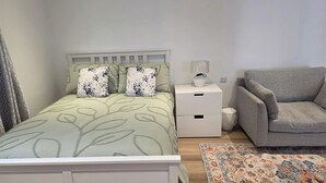 Ein Schlafzimmer mit einem Bett, einem Nachttisch, einer Lampe, einem grauen Sessel und einem gemusterten Teppich.