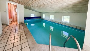 Une piscine intérieure avec un sol carrelé, un bord bleu et un plafond en bois.