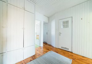 A hallway with white paneling, wooden flooring, and a door with a window. - Osiedle Batorego Colorful Apartment (Poznań)