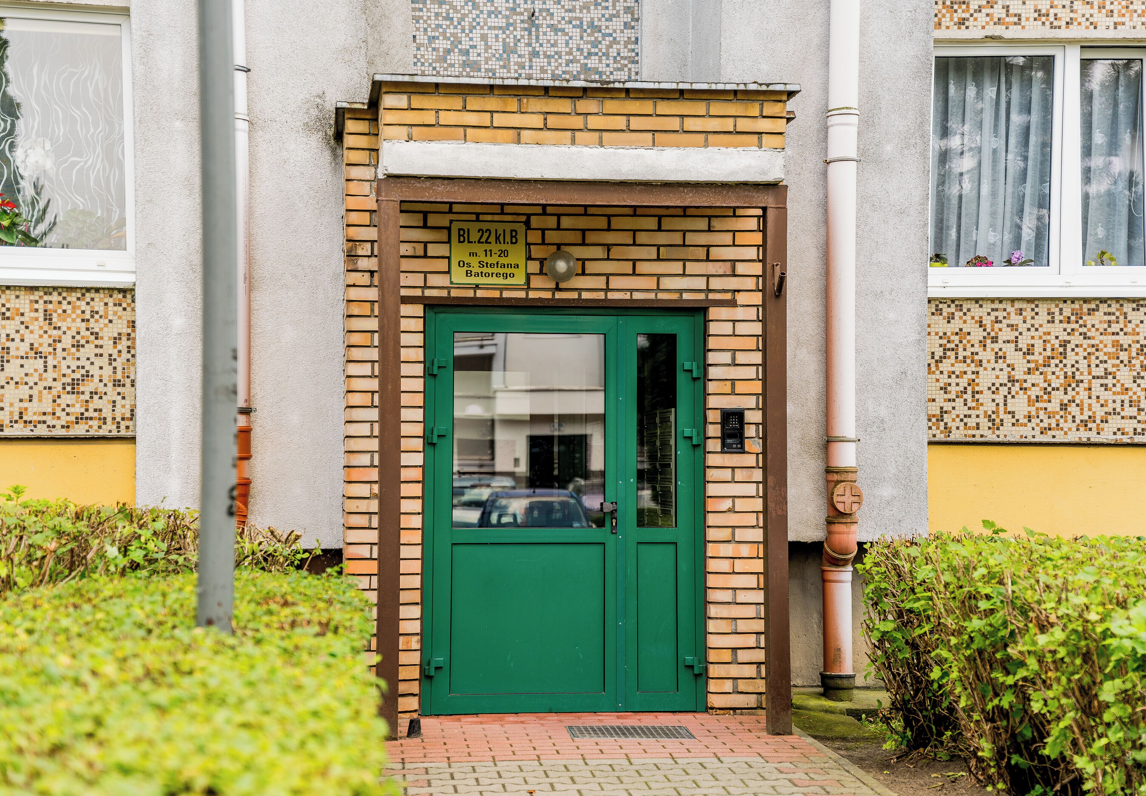 A green door with a sign above it, a tiled wall, and a window with curtains.