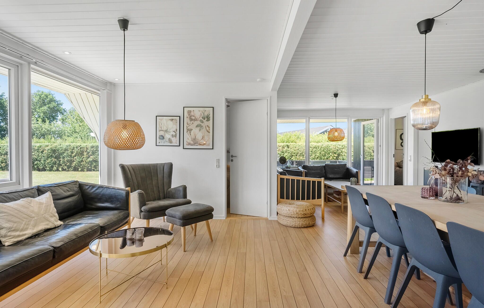Een modern interieur met een houten vloer, een bank, een eettafel met stoelen en uitzicht door een glazen deur.