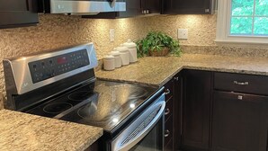 A modern kitchen with dark cabinetry, stainless steel appliances, granite countertops, and a window with a view of greenery. - Hawthorne Hill (Brevard)