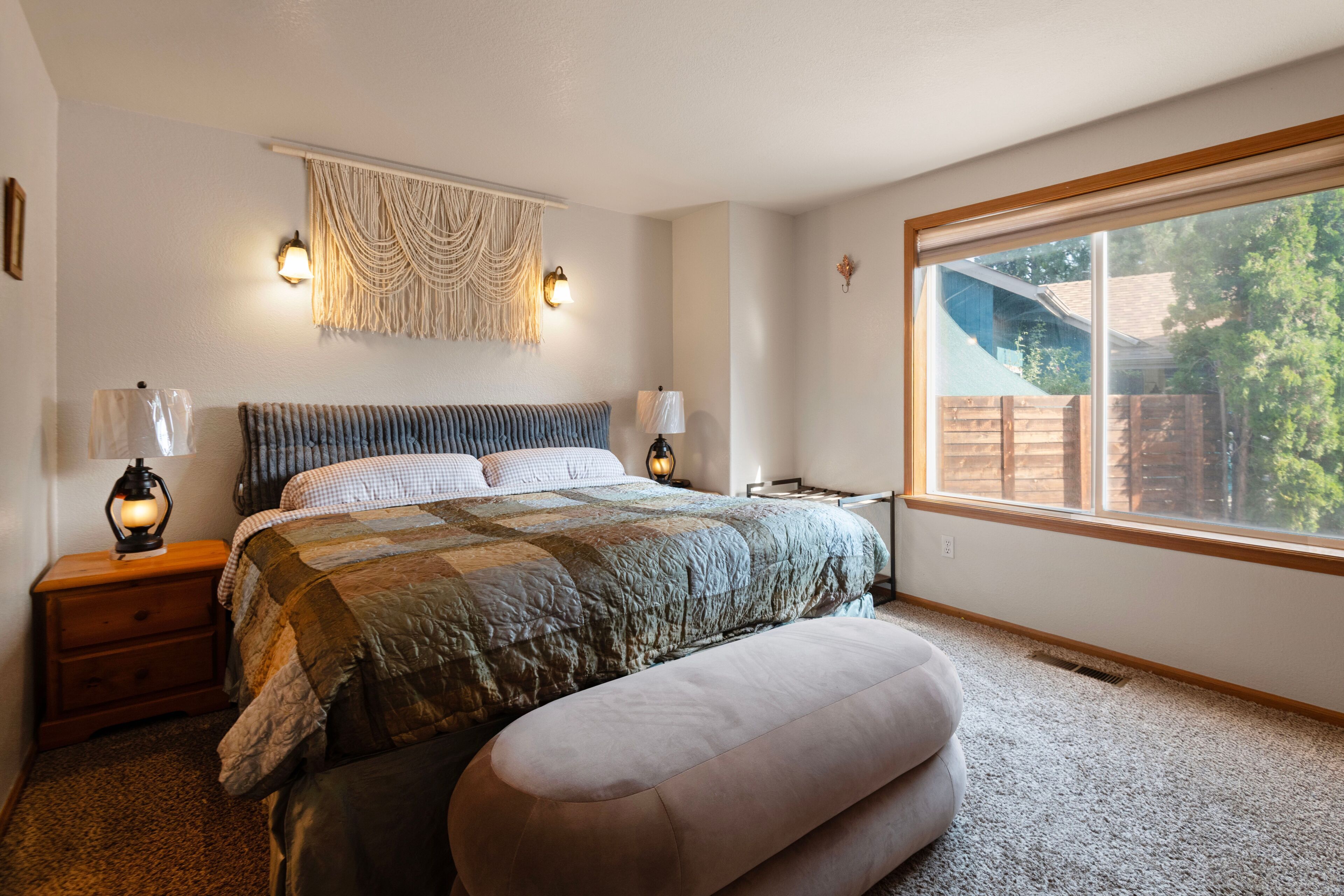A bedroom with a large bed, bedside lamps, a wall-mounted macrame, and a window with a view of the outdoors.