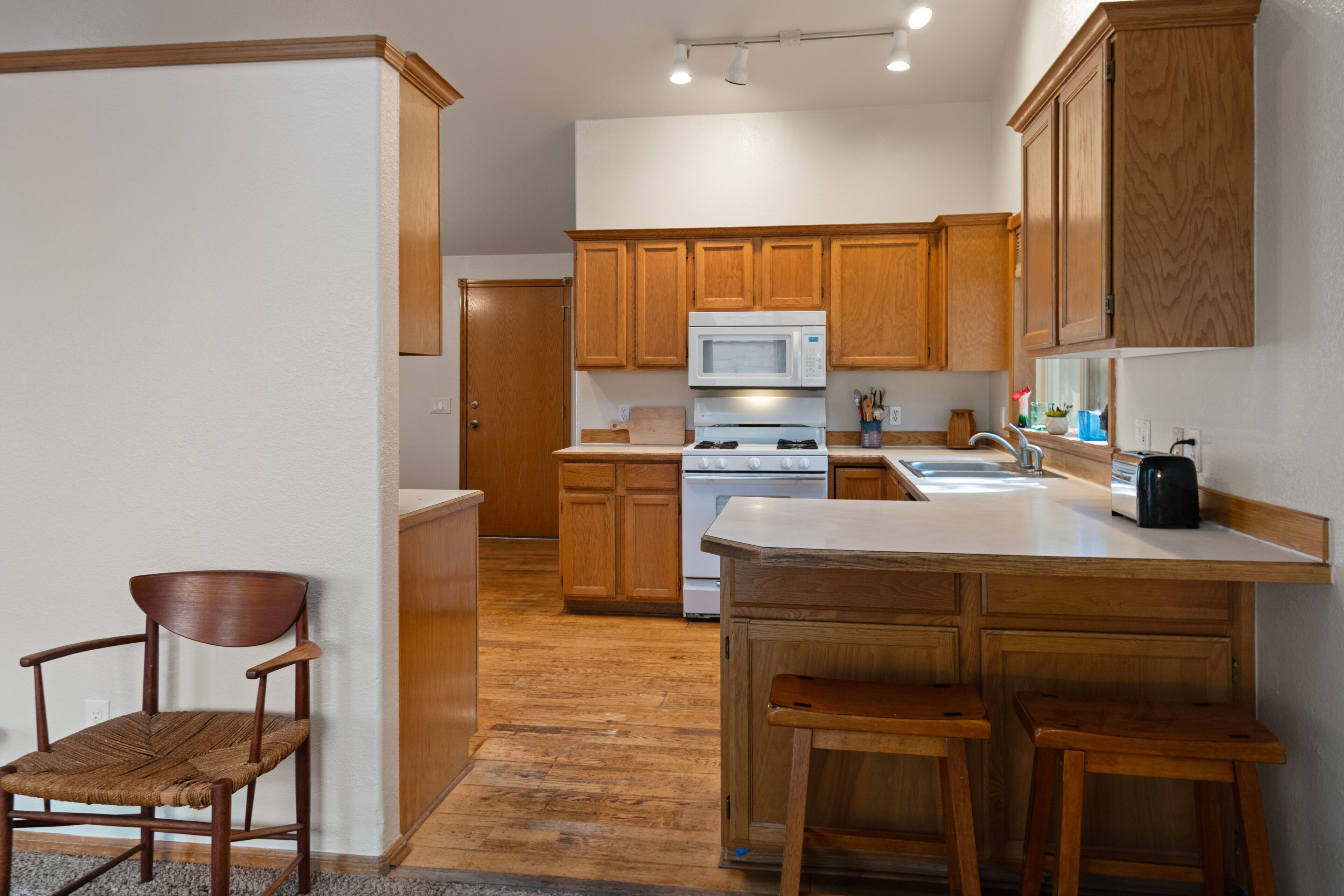 A kitchen with wooden cabinets, a white stove, and a microwave. There is a chair and a small table.