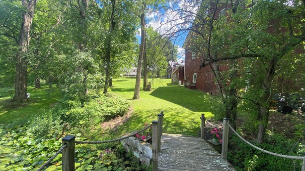 A wooden bridge leading to a grassy area with a red building in the background.