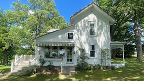 A white two-story house with a porch, steps, and a small garden.