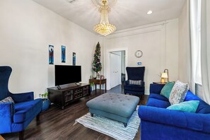 Una sala de estar con televisor, dos sofás azules, una mesa de centro, una araña y un árbol de Navidad.