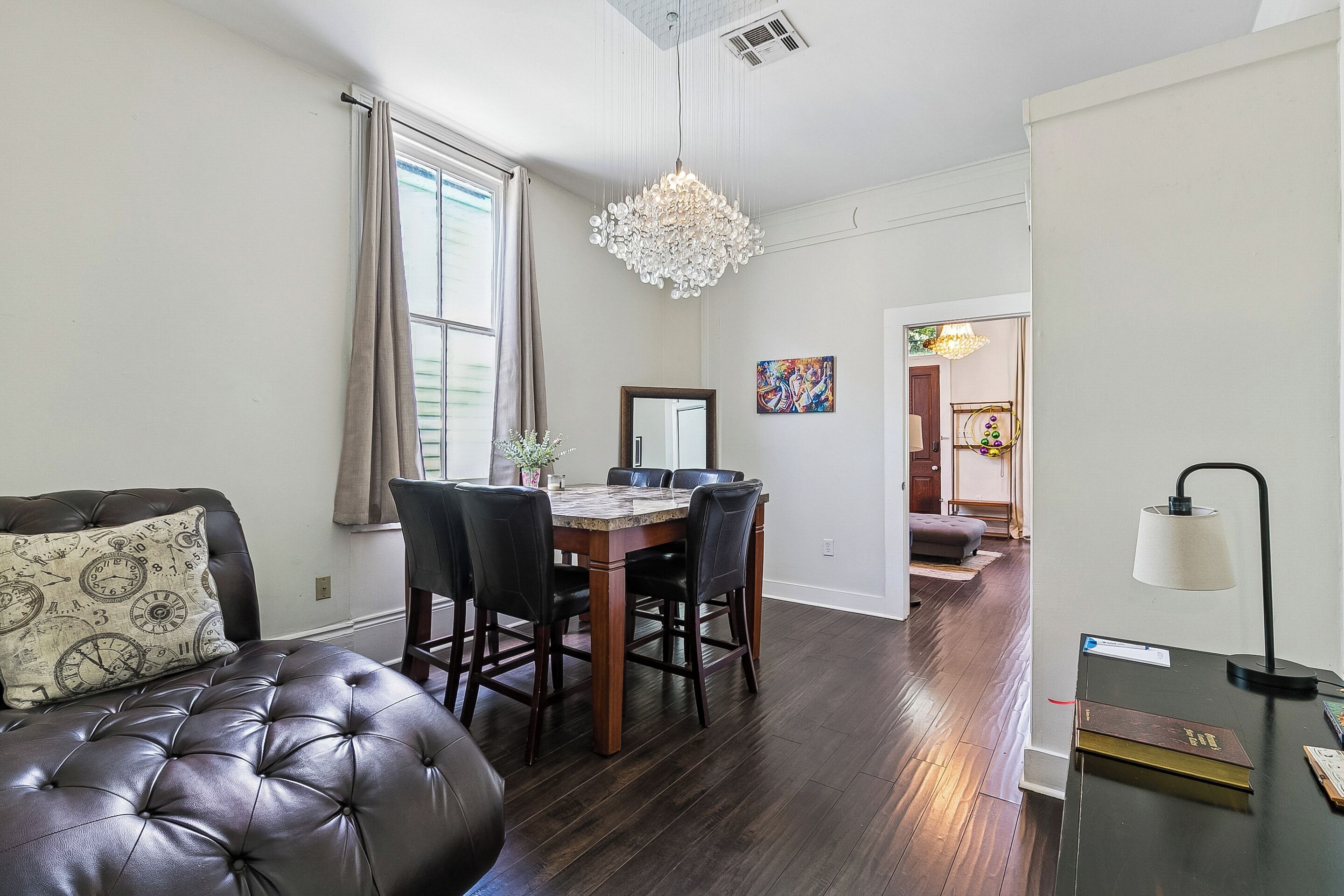 A dining area with a wooden table and chairs, a chandelier, and a view into another room.
