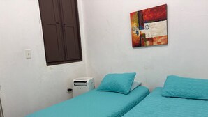 Ein kleines, sauberes Zimmer mit zwei Betten, einem Heizkörper, einem Wandbild und einem Fenster mit einem braunen Rollo.