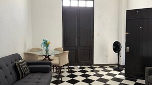 Ein Zimmer mit Schachbrettboden, einem dunklen Sofa, einem Esstisch mit Stühlen und einer schwarzen Tür.