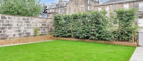 A well-maintained garden with a stone wall, neatly trimmed hedges, and a grassy lawn.