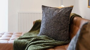 Ett rum med en soffa klädd i läder, en grön pläd och en vit golvlampa.