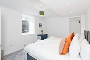 A bedroom with a bed, a window, a radiator, a nightstand, and a door. - GuestReady - 2bed w Private Patio in Edinburgh (Edinburgh)