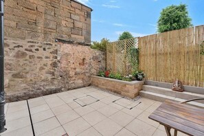 A patio area with stone walls, a wooden fence, and a bench. - GuestReady - 2bed w Private Patio in Edinburgh (Edinburgh)