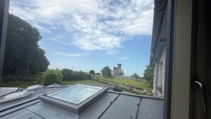 Une terrasse sur le toit avec une lucarne, une vue sur un château et un paysage verdoyant.