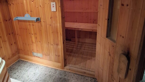 Interno di una baita di legno con una panca, una porta che dà su un'altra stanza e un piccolo oblò.