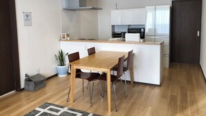 A modern kitchen with white cabinets, a wooden dining table, and a built-in island with seating. - Minami Ward, Sapporo—10 or more people / Free shuttle service available / Perfect for groups and families with children! Free parking for 4 cars / We can arrange rental cars! (札幌市minami-ku,fujino)