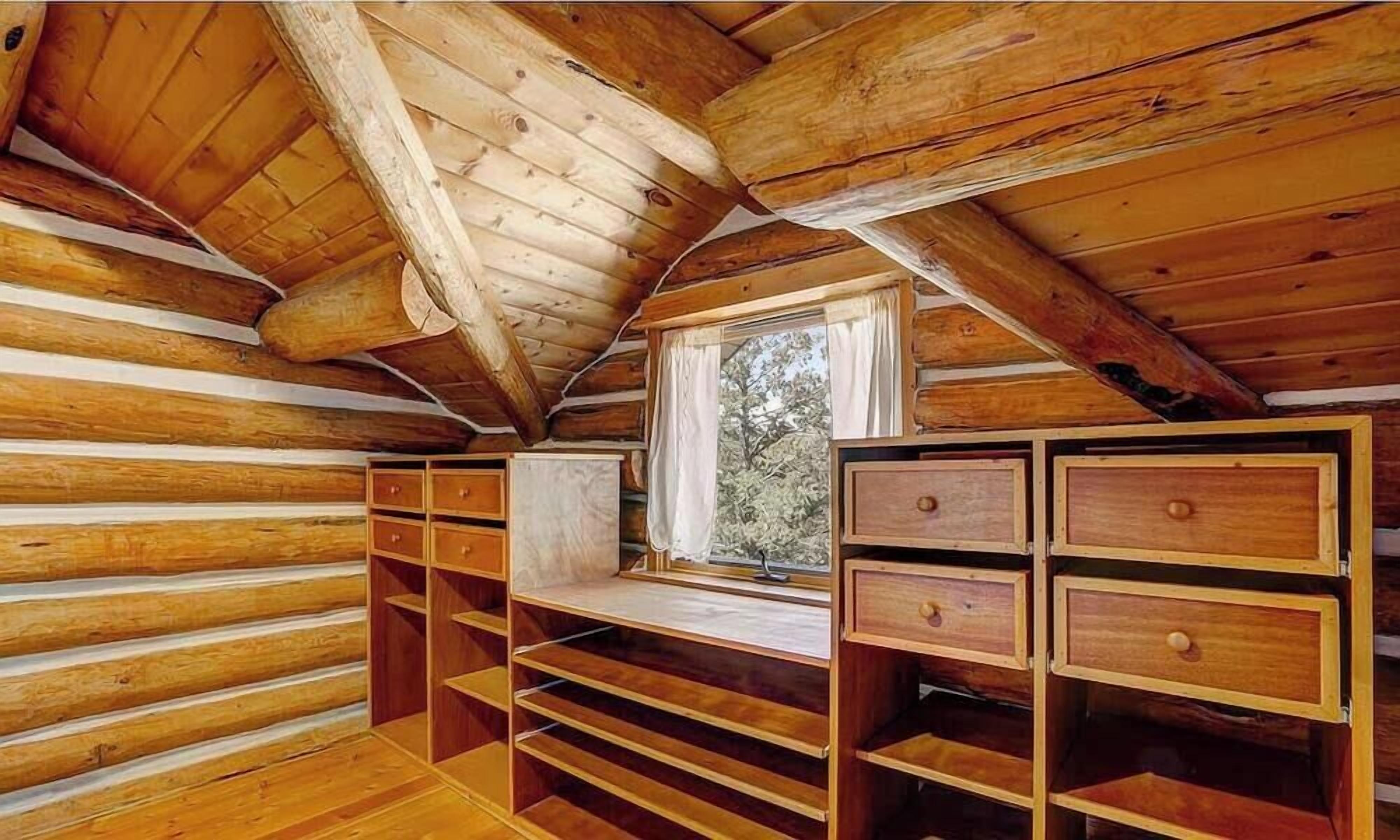 Un intérieur en bois avec un plafond en pente, des étagères intégrées et une fenêtre donnant sur la forêt.