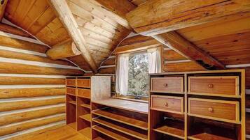 Un intérieur en bois avec un plafond en pente, des étagères intégrées et une fenêtre donnant sur la forêt.