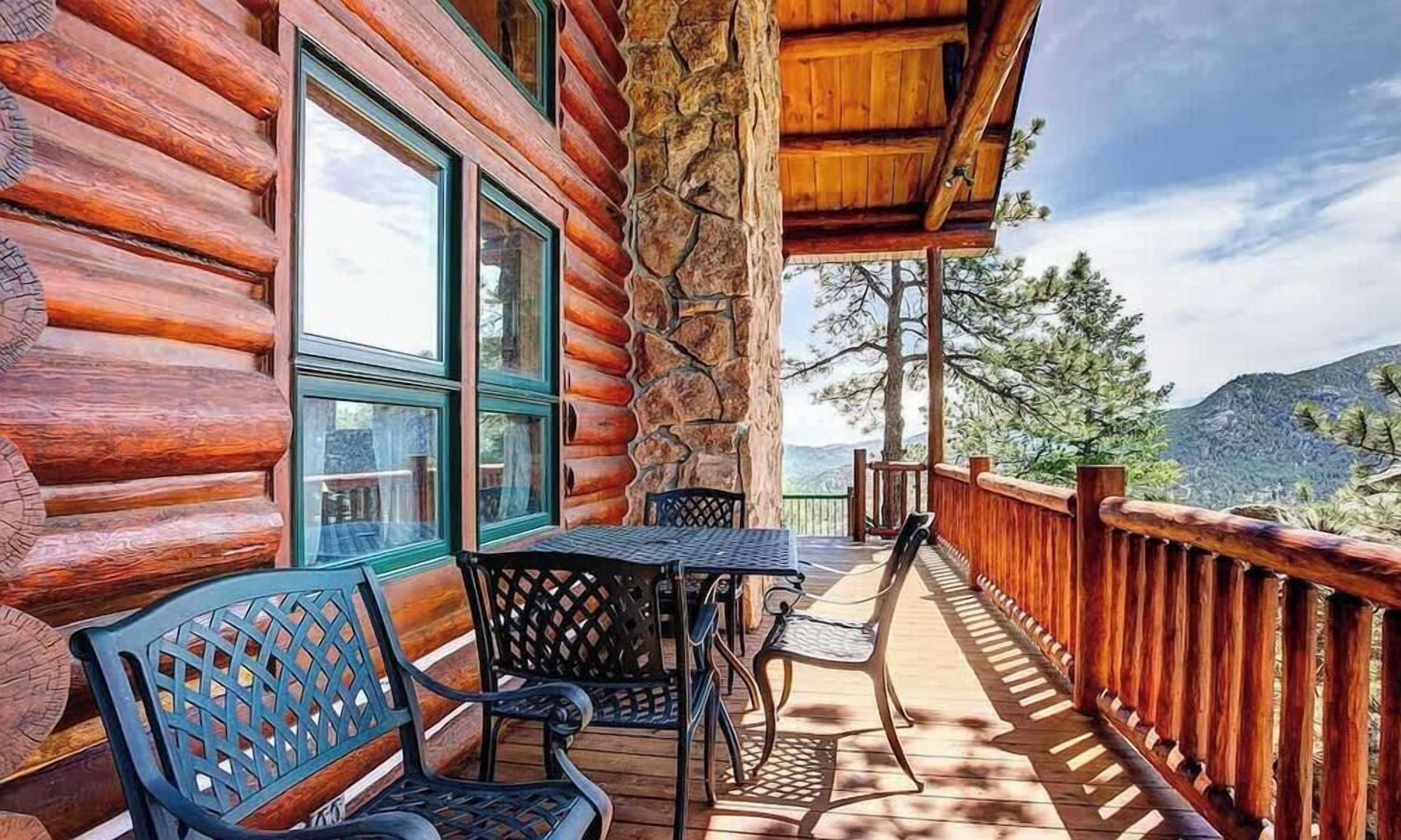 Une cabane en rondins avec une terrasse en bois, un espace salon extérieur et une vue sur les montagnes.