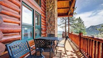 Une cabane en rondins avec une terrasse en bois, un espace salon extérieur et une vue sur les montagnes.