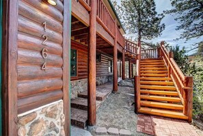 A wooden cabin with a stone foundation, a porch with wooden railings, and a staircase leading to the upper level. - Range View on the Rocks | Log Home | 360 Mtn Views (Estes Park)