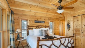 A wooden cabin bedroom with a bed, a 'DO NOT FEED THE BEARS' sign, a lamp, and a window with blinds. - Sunny Rise Cabin | Hot Tub, Pet Friendly, Fire Pit & Views! (Rutherfordton)