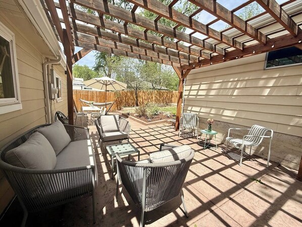 Eine überdachte Terrasse mit Korbmöbeln, einem kleinen Tisch und einem Stuhl.