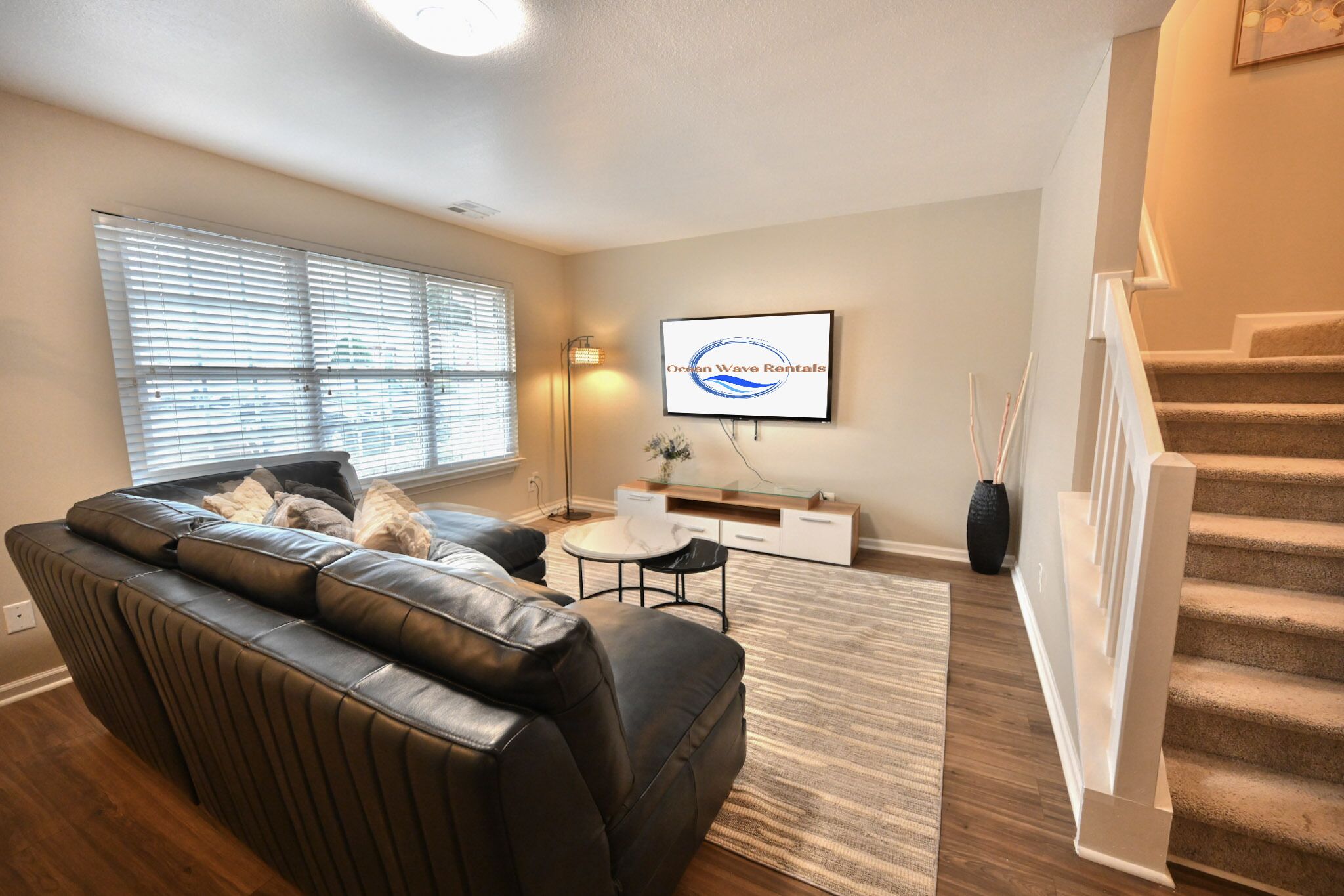 A living room with a leather sofa, a flat-screen TV, a small table, and a staircase.