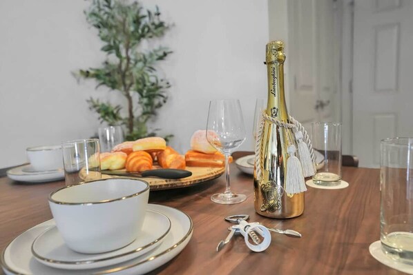 Un tavolo apparecchiato con una bottiglia di champagne, calici, piatti con pasticcini e una ciotola.