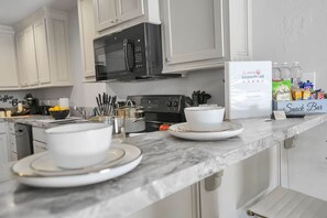 A kitchen with white cabinets, a black stove, and a countertop with a coffee machine, utensils, and a Superhost sign. - Roomy Townhome - 15 mins to Fort Sill, Wichitas #A (Elgin)