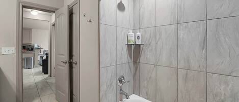 Une salle de bain avec une baignoire, une douche et des toilettes. On trouve des articles de toilette sur une étagère.