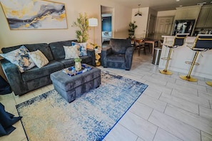 A living room with a sofa, armchair, and ottoman, a dining area with a table and chairs, and a kitchen with bar stools. - Roomy Townhome - 15 mins to Fort Sill, Wichitas #A (Elgin)